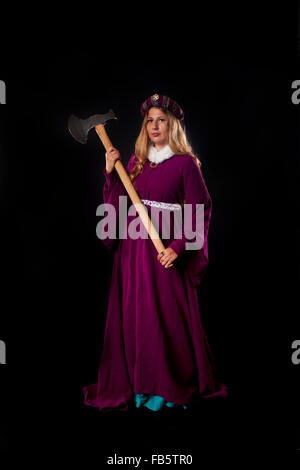 Studio photo de belle fille vêtue comme une noble dame médiévale en violet manteau avec grosse hache sur fond noir Banque D'Images