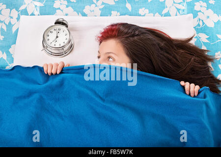 Portrait of a young woman Lying in Bed, se cachant sous une couverture bleue à la recherche et le réveil. Étudiant n'a pas envie de se réveiller tôt. Banque D'Images