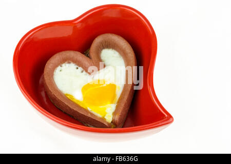 Avec un oeuf de saucisses en forme de cœur en rouge sur la plaque en forme de cœur isolé sur fond blanc Banque D'Images