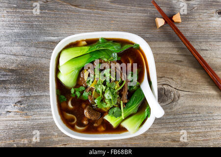 Angle de vue élevé Nouilles en soupe au bœuf le bok choy et le persil. En soupe soupe avec des baguettes dans le support sur bois rustique. Banque D'Images