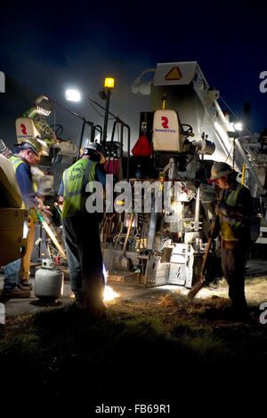 Les travailleurs se tiennent derrière un épandeur d'asphalte mélangé à chaud mise en route inter-États de travailler de nuit. Banque D'Images