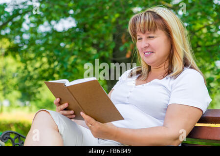 Femme mature la lecture d'un roman tout en étant assis sur un banc de parc Banque D'Images