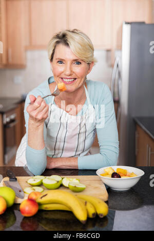 Femme mature en bonne santé de manger de la salade de fruits à la maison Banque D'Images