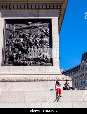 Londres, Trafalgar Square, deux jeunes touristes femme avec les téléphones intelligents à la base de la Colonne Nelson Banque D'Images
