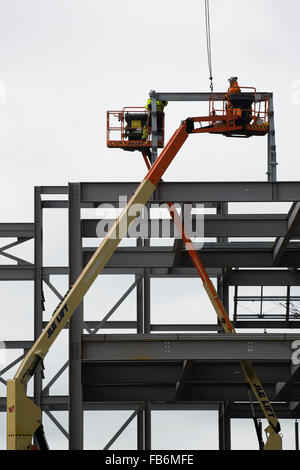 Les travaux de construction au Royaume-Uni : les hommes travaillent en hauteur sur des plates-formes 'cherry picker', boulonnage ensemble le cadre en acier d'un nouveau développement pour le supermarché Tesco et Marks & Spencer store sur un chantier à Aberystwyth, Pays de Galles, Royaume-Uni Banque D'Images