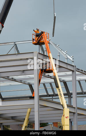 Les travaux de construction au Royaume-Uni : les hommes travaillent en hauteur sur des plates-formes 'cherry picker', boulonnage ensemble le cadre en acier d'un nouveau développement pour le supermarché Tesco et Marks & Spencer store sur un chantier à Aberystwyth, Pays de Galles, Royaume-Uni Banque D'Images