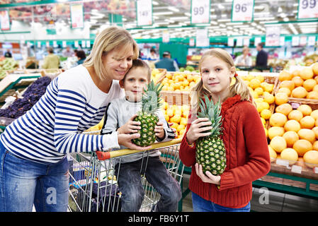 Mère et enfants avec fruits ananas en ministère dans le supermarché Banque D'Images