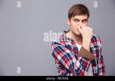 Irrité beau jeune homme en chemise à carreaux couverts son nez à cause de mauvaise odeur sur fond gris Banque D'Images