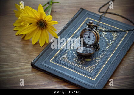 Vintage montre de poche et fleur jaune allongé sur le vieux livre Banque D'Images