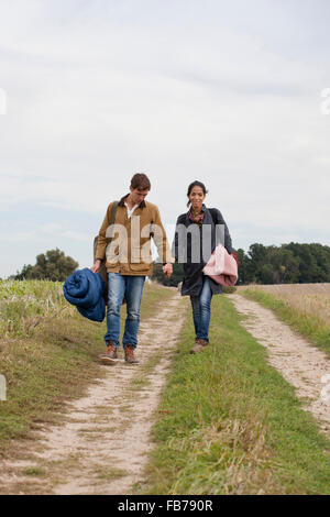 Jeune couple carrying accessoires de camping marche à travers un chemin de terre Banque D'Images