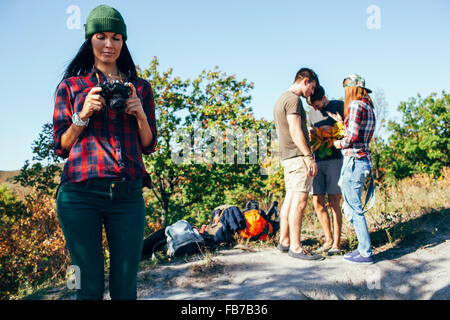 Jeune femme à la recherche de photographies sur l'appareil photo avec les amis standing in forest Banque D'Images