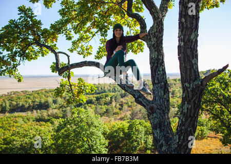 Full Length portrait of young woman sitting on tree in forest Banque D'Images