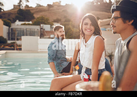Portrait de la belle jeune femme assise au bord de la piscine avec ses amis autour de la fête. Groupe de jeunes gens en suspens autour d'un s Banque D'Images