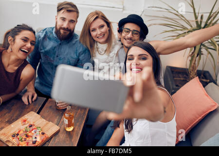 Les gens s'amuser à multiraciale partie prenant une avec selfies téléphone mobile. Groupe de jeunes amis sitting on couch taking self po Banque D'Images