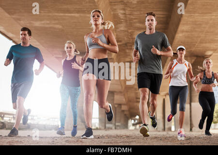 Groupe déterminé de jeunes fonctionnant ensemble en ville. Low angle view of running club membres formation ensemble dans la matin Banque D'Images