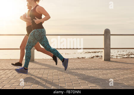 Cropped shot de deux jeunes femmes en marche le long d'une promenade en bord de mer. De jeunes coureurs travaillant ensemble sur une route par le s Banque D'Images