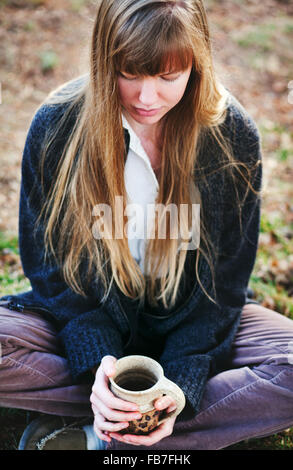 Jeune femme assise sur le sol en regardant grande tasse de liquide chaud Banque D'Images