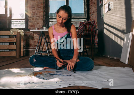 Woman painting while sitting on floor in art studio Banque D'Images