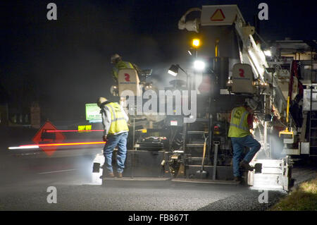 Les travailleurs se tiennent derrière un épandeur d'asphalte mélangé à chaud plaçant pendant les travaux routiers inter-Etats. Banque D'Images