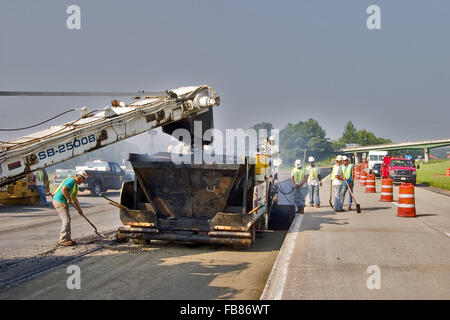 Le mélange d'asphalte chaud étant chargé dans un épandeur et mis sur la route par des travailleurs de la construction. Banque D'Images