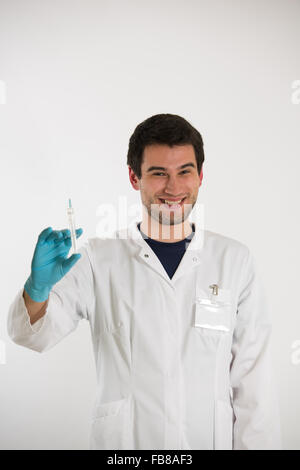 Jeune homme médecin, sur fond blanc, vêtu de blanc et bleu gants, détient seringue Banque D'Images