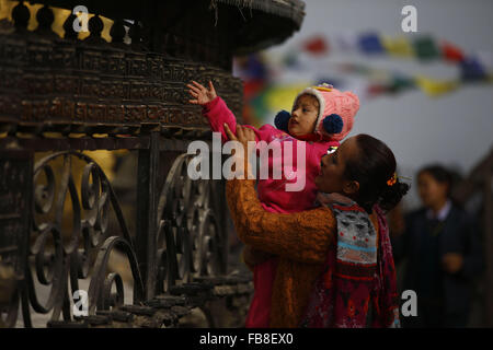 Katmandou, Népal. 12 Jan, 2016. Une mère enfant permet de faire tourner les roues de prière à l'Swayambhunath Stupa locaux à Katmandou, Népal, le mardi 12 janvier, 16. Swayambhunath est aussi connu sous le nom de Monkey Temple comme il y a des singes saint vivant dans la partie nord-ouest du temple. Il a été inscrit dans la liste de monument du patrimoine mondial de l'en 1979. © Skanda Gautam/ZUMA/Alamy Fil Live News Banque D'Images