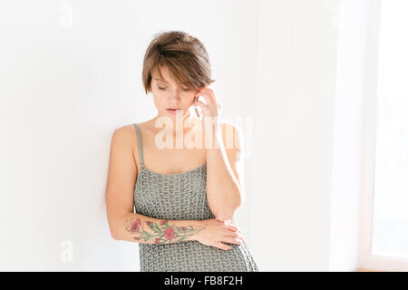 Une jeune femme avec coupe courte et tatoo sur la main à l'aide de téléphone sur fond blanc Banque D'Images