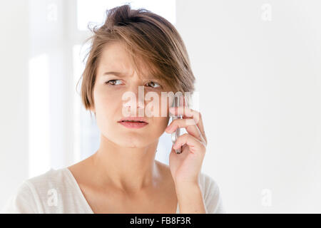 Inquiets troublée young woman talking on mobile phone over white background Banque D'Images