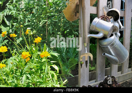 Arrosoirs en métal accrochée à une clôture dans un jardin potager Banque D'Images