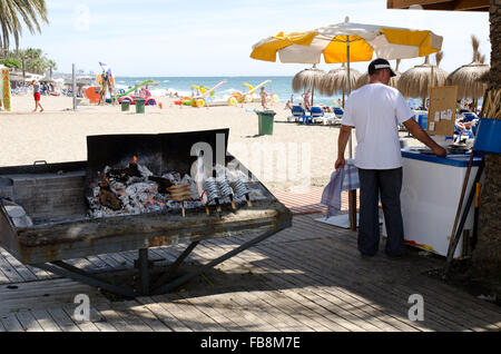 Lignes d'anchois et de sardines sur des brochettes en bois cuisson sur un barbecue sur la plage Playa de la Vénus à Marbella Banque D'Images