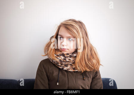 Belle blonde Caucasian teenage girl sitting on outwear chaud canapé bleu sur mur blanc Banque D'Images