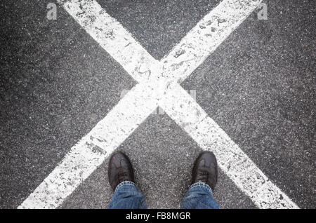 Pieds masculins debout sur l'asphalte urbain sombre avec des lignes de passage de la signalisation horizontale Banque D'Images