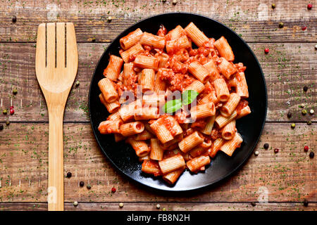 High angle shot d'une plaque noire avec penne rigate à la sauce bolognaise sur une table en bois rustique Banque D'Images