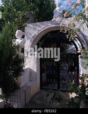 Portes en fer forgé orné sous arche blanche avec un buste classique et rose rosiers grimpants en grande jardin espagnol Banque D'Images