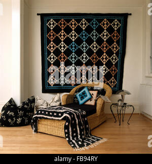 Tenture murale tapis tissé dans la salle de séjour avec un noir +laine blanc jeter sur une chaise longue en osier Banque D'Images