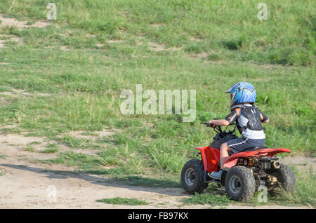 Boy Riding un Quad ATV rouge sur un chemin de terre sèche un jour d'été Banque D'Images