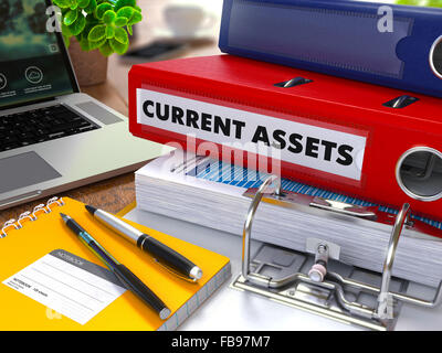 Classeur rouge avec l'inscription de l'actif sur la table de travail de fond avec les fournitures de bureau, ordinateur portable, des rapports. Tonique Illu Banque D'Images