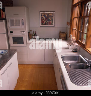 Acier inoxydable double vasque et parquet dans une cuisine blanche avec four double au niveau de l'oeil Banque D'Images