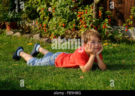 Boy lying on grass, reposant la tête dans les mains, à la réflexion Banque D'Images