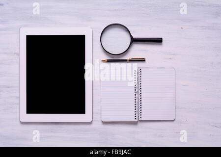 Ordinateur portable, tablette, loupe et un stylo sur la table en bois blanc. Vue du dessus avec copyspace. Banque D'Images