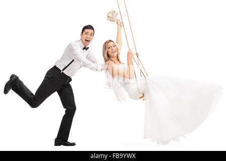 Jeune homme joyeux poussant sa jeune femme sur une balançoire isolé sur fond blanc Banque D'Images