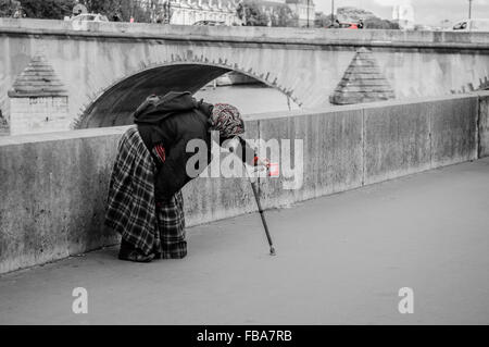 Une vieille femme sans-abri, s'appuyant sur un bâton de marche de soutien, près d'un pont sur la Seine à Paris, à la mendicité pour l'argent. Une image en noir et blanc avec un petit rouge de l'isolement Banque D'Images