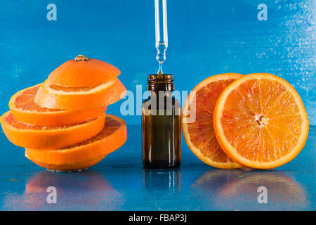 L'huile essentielle d'orange flacon compte-gouttes avec ambre et les tranches d'orange douce, avec fond bleu Banque D'Images