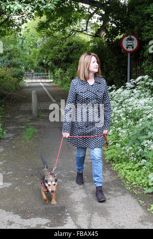 Femme portant un manteau tacheté petit chien marche le long sentier au printemps Banque D'Images