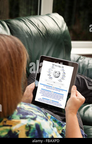 Une femme lisant Wikipedia en ligne sur un ordinateur tablette iPad à la maison, UK Banque D'Images