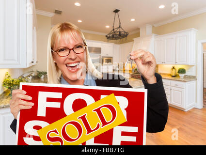 Happy Young Woman Holding a vendu Achat Immobilier signe et clés à l'intérieur de belle cuisine sur mesure. Banque D'Images