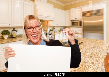 Happy Young Woman Holding Blank Sign et clés à l'intérieur de belle cuisine sur mesure. Banque D'Images