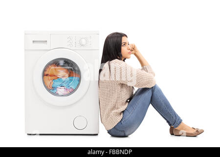 Jeune femme pensive assise sur le sol en attendant le lave-linge pour terminer isolé sur fond blanc Banque D'Images