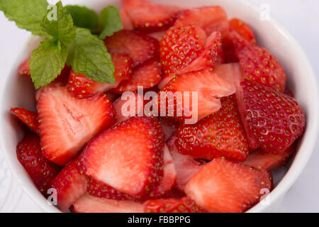 Vue aérienne aromatiques fraîches fraises rouge coupé en fines tranches. Dans les fruits sains bol blanc avec des feuilles de menthe verte Banque D'Images