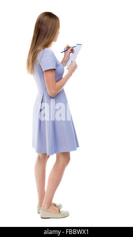 Vue arrière de la femme se prend des notes sur un ordinateur portable. girl. Vue arrière Vue arrière. collection les gens de personne. Plus isolé sur fond blanc. La jeune fille dans une robe bleue se dresse sur le côté et s'appuie sur un ordinateur portable. Banque D'Images